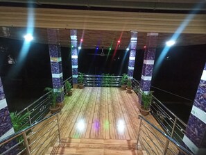 Une terrasse en bois avec des rampes, des plantes en pot et une scène éclairée de couleurs vives.