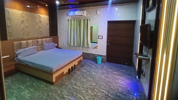 Un dormitorio con una cama, ventilador de techo, unidad de aire acondicionado, televisión y una puerta.