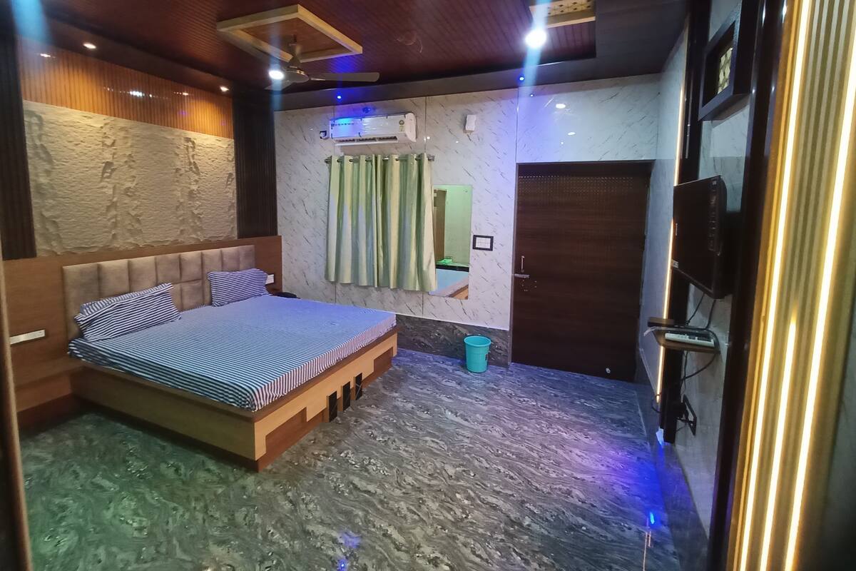 A bedroom with a bed, a ceiling fan, an air conditioning unit, a television, and a door.