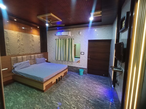 Une chambre à coucher comprenant un lit, un ventilateur de plafond, un appareil de climatisation, un téléviseur et une porte.