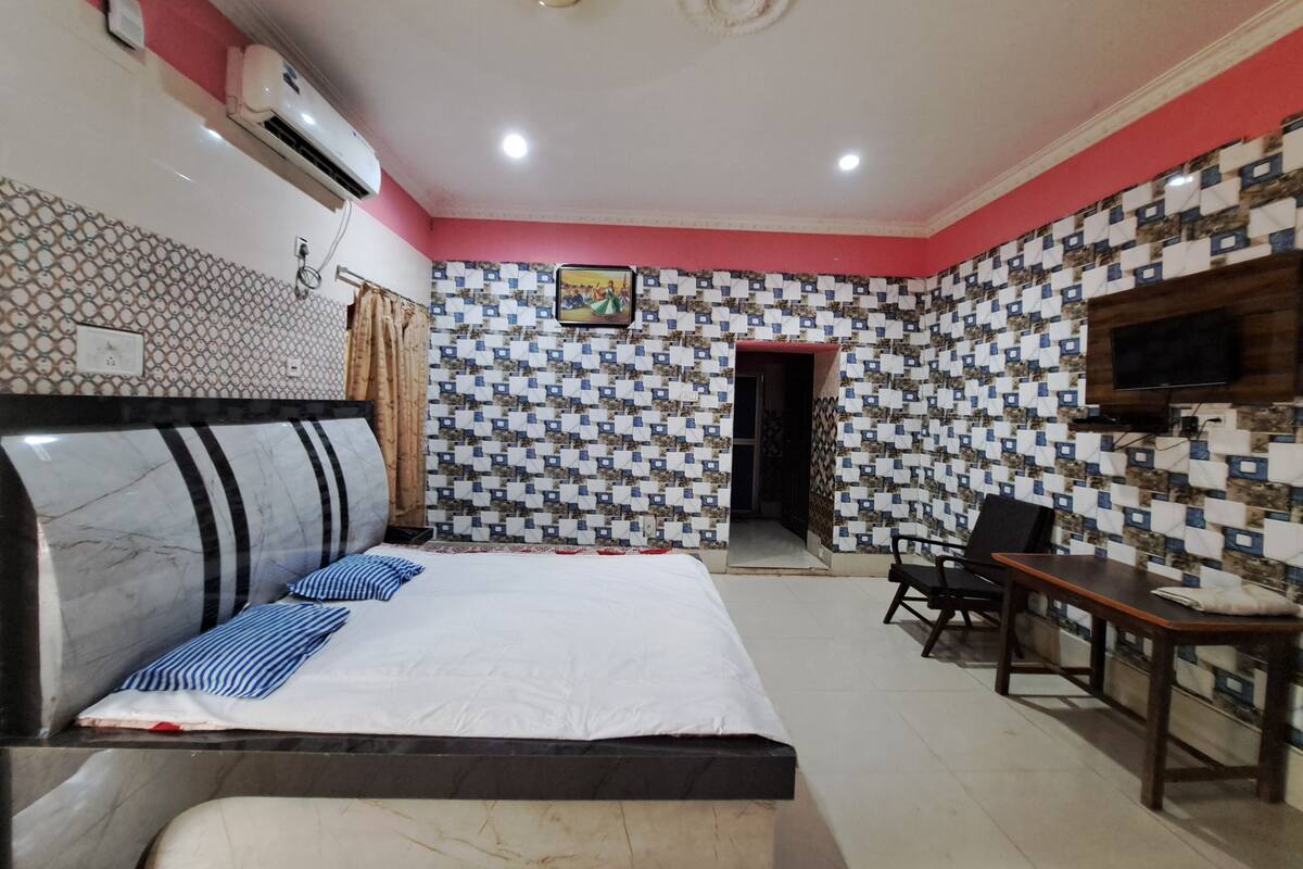 A hotel room with a bed, a desk, a chair, a TV, and a patterned wall.
