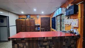 A reception area with a red counter, wooden cabinets, a fan, and a wall-mounted clock. - Khairi Resort (Bangriposi)