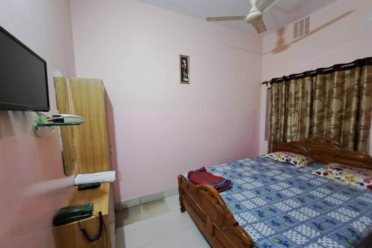 A bedroom with a bed, a wooden wardrobe, a television mounted on the wall, and a ceiling fan.