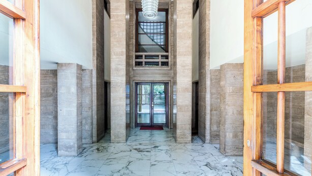 A hallway with marble flooring, wooden columns, and a glass door at the end.