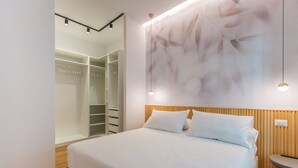 A modern bedroom with a large bed, a walk-in closet, and a wall-mounted light fixture.