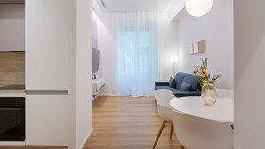 A modern living room with a white sofa, a round dining table, and a vase with flowers.