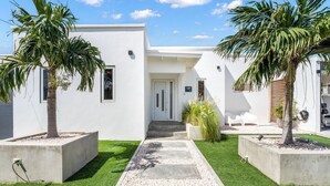 A modern building with a white facade, a concrete pathway leading to the entrance, and two palm trees in planters.