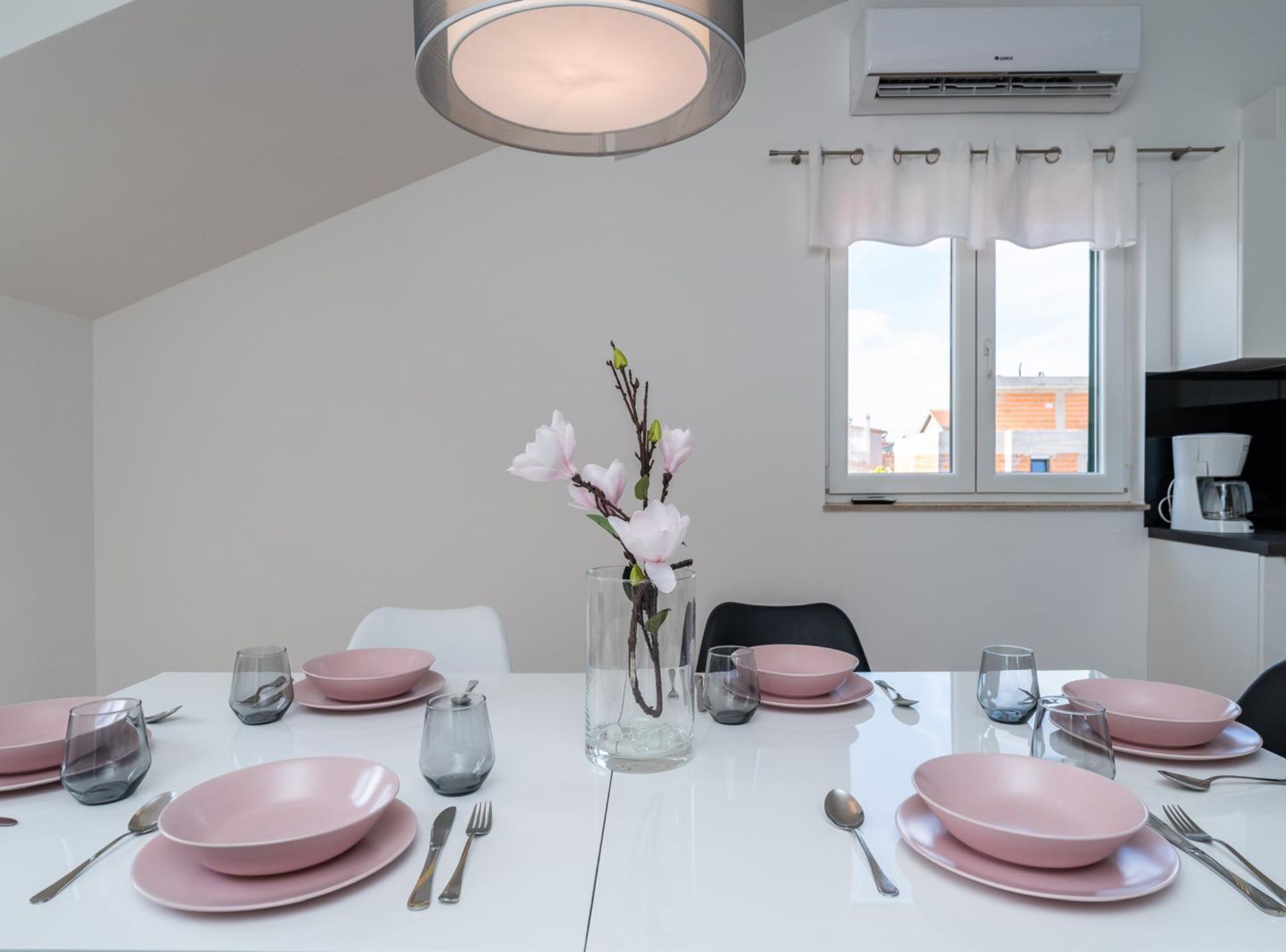 Een eetkamer met roze borden, heldere glazen en een vaas met bloemen.