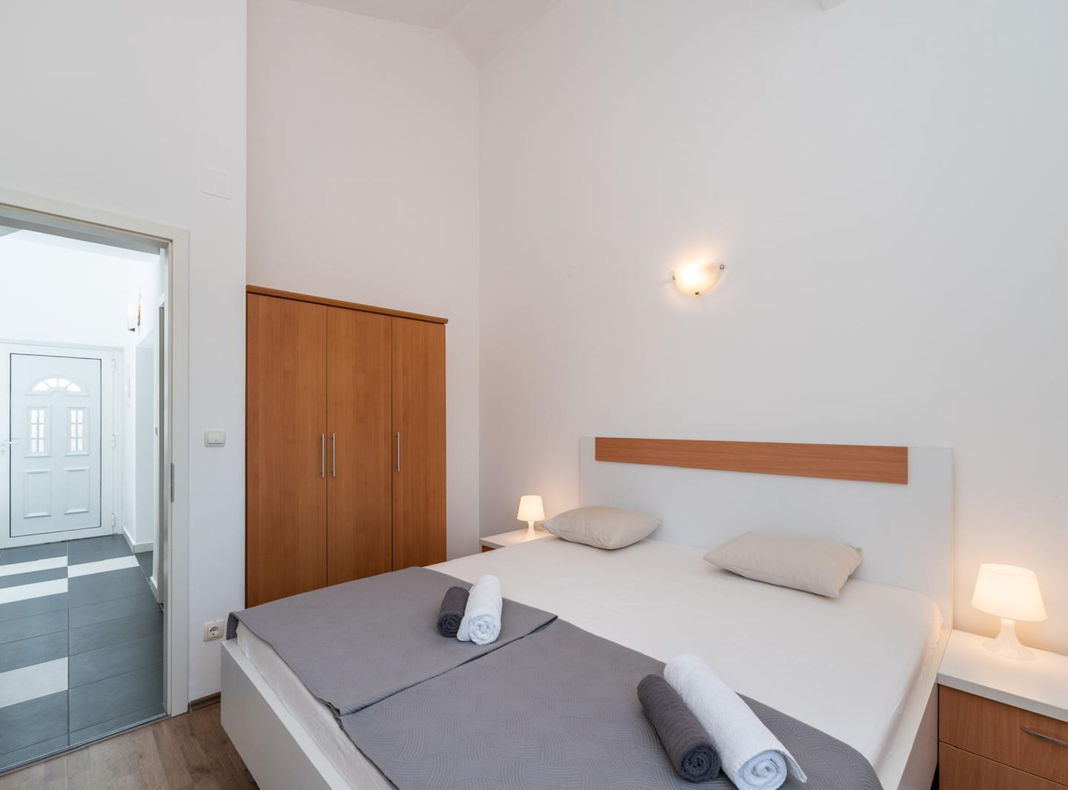 A hotel room with a bed, bedside lamps, a wardrobe, and a door to the outside.