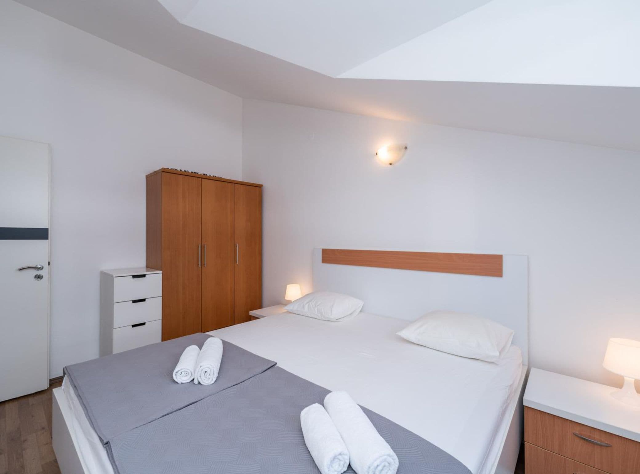 Une chambre d’hôtel moderne équipée d’un lit, d’une armoire, d’une table de chevet avec une lampe et d’une applique murale.