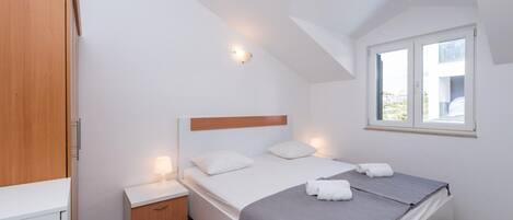 A bedroom with a bed, bedside table, lamp, and a window with a view.