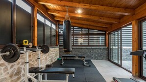 Un gimnasio con pared de piedra, techo de madera y grandes ventanales con vistas a un cuerpo de agua.