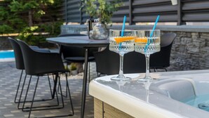 Un área junto a la piscina con un jacuzzi, dos vasos con rodajas de naranja y una mesa con sillas.