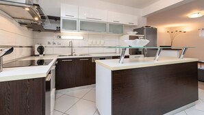 Una cocina moderna con armarios blancos, una isla con encimera de vidrio y electrodomésticos de acero inoxidable.