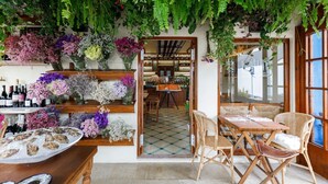 A restaurant with a bar area, wooden furniture, and a variety of flowers and plants on the walls.