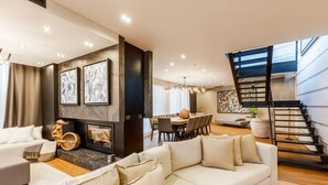 A modern living room with a fireplace, a dining area, and a staircase.