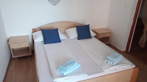 Parivuode, jossa on kaksi tyynyä, puinen yöpöytä ja pieni sivupöytä, jossa on lamppu.