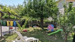 A backyard with a white plastic chair, a swing set, a small tree, and a playhouse. - Room in Lopar with Balcony, WIFI (4620-94) (Lopar)