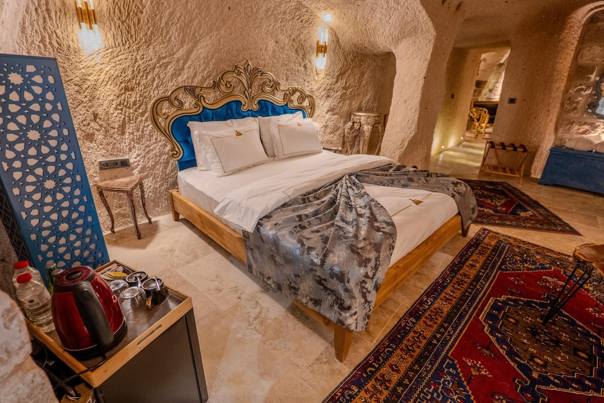 Un dormitorio con pared de piedra, una cama con cabecera azul, una mesita de noche de madera, un hervidor rojo y un panel decorativo azul.