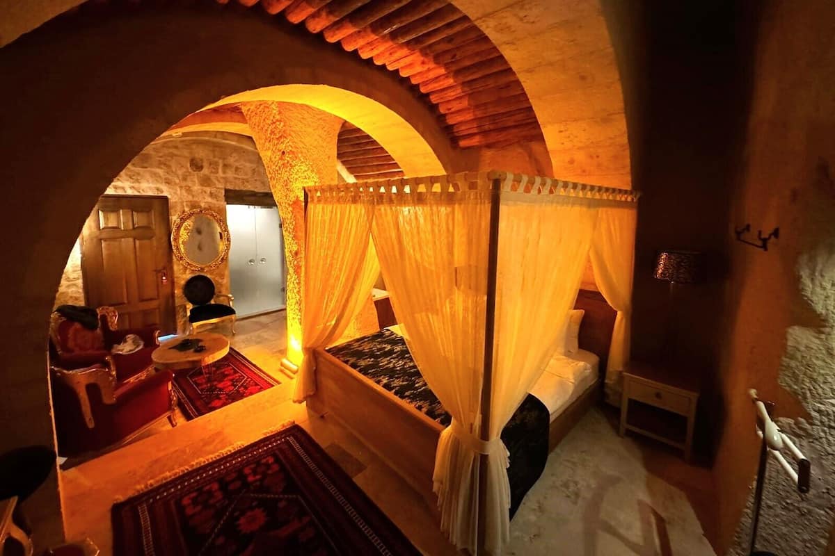Una habitación acogedora con cama con dosel, techo de madera y pared de piedra. Hay una pequeña mesa con una silla y una alfombra en el suelo.