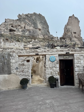 A stone building with a reception area, a staircase leading up, and a view of a rocky mountain in the background. - Patina Cappadocia (Nevsehir)
