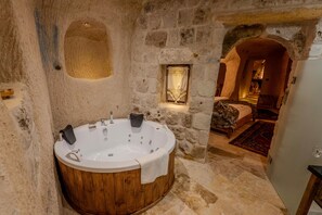 A stone-walled bathroom with a wooden bathtub, a small window with a curtain, and a bed visible through an archway. - Patina Cappadocia  (Nevsehir)