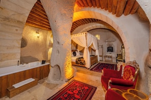 A room with a stone wall, wooden ceiling, a bathtub, a bed with a canopy, and a red chair. - Patina Cappadocia (Nevsehir)