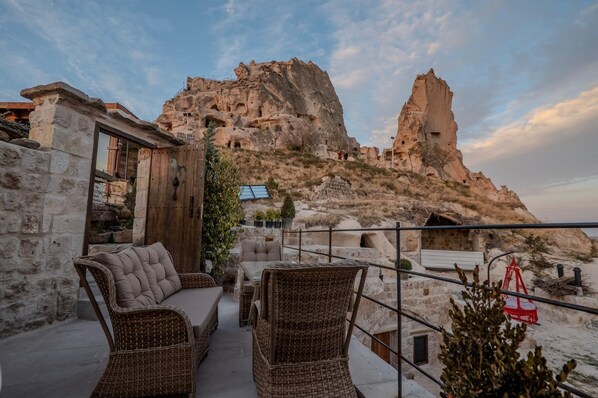 A terrace with wicker furniture, a stone wall, and a view of a rocky mountain. - Patina Cappadocia (Nevsehir)
