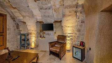 A stone-walled room with a leather armchair, a wooden table, and a television mounted on the wall.