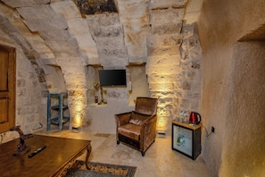 A stone-walled room with a leather armchair, a wooden table, and a television mounted on the wall. - Patina Cappadocia (Nevsehir)