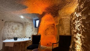 A rustic interior with a stone wall, a round wooden table, two chairs, and a small window. - Patina Cappadocia  (Nevsehir)