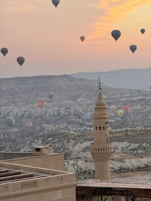 A view of a cityscape with a prominent minaret in the foreground and numerous hot air balloons in the background. - Patina Cappadocia  (Nevsehir)
