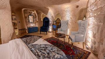 A cozy, cave-like room with a bed, two armchairs, a small table, and a decorative mirror.