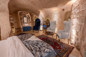 A cozy, cave-like room with a bed, two armchairs, a small table, and a decorative mirror. - Patina Cappadocia (Nevsehir)