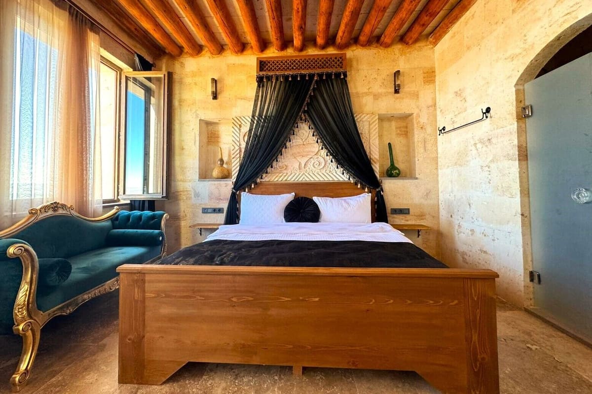 Un dormitorio con una cama de madera, un sillón verde y una ventana con cortinas.