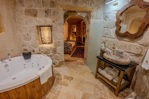 A stone-walled bathroom with a wooden bathtub, a stone sink, and a mirror. - Patina Cappadocia (Nevsehir)