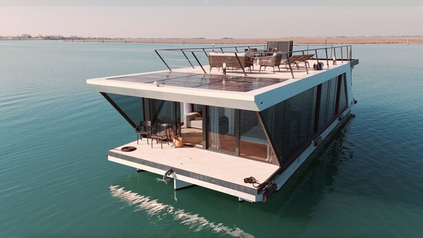 A modern floating house with a deck, glass walls, and a view of the water.