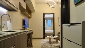 A modern kitchen with wooden cabinets, a stainless steel sink, and a built-in oven. There is a small dining area with a table and chairs, and a TV mounted on the wall. - Taguig Grand Suite - Cozy Modern Apartment (Taguig)