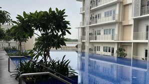 A modern hotel with a rooftop infinity pool, surrounded by lush greenery and a multi-story building with balconies. - Taguig Grand Suite - Cozy Modern Apartment (Taguig)