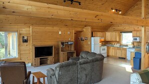 Un salón amplio con un sofá seccional gris grande, techo de madera y una zona de cocina con armarios de madera y un microondas.