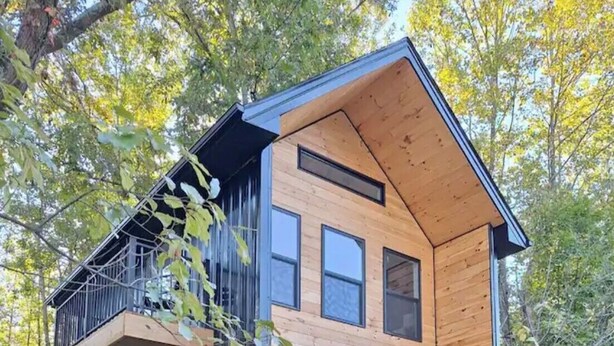 Ein modernes, zweistöckiges Haus mit Holzfassade, einem Balkon im oberen Geschoss und einer Garagentür.