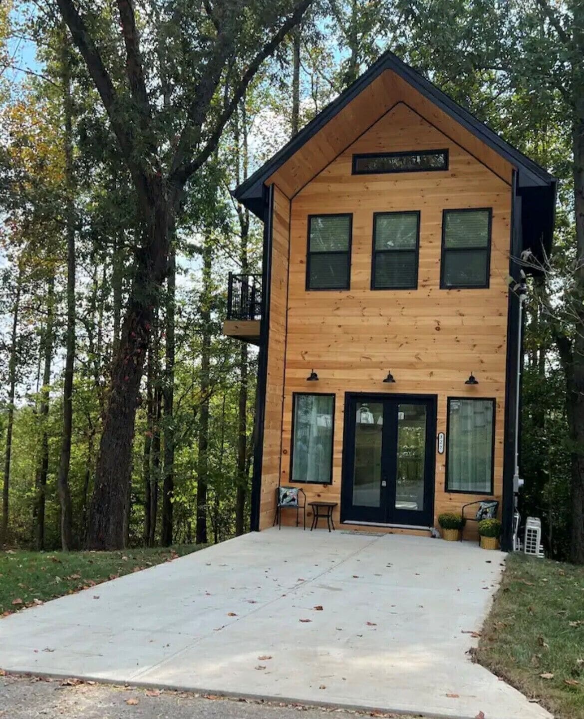 A two-story wooden cabin with a front porch, large windows, and a black roof.
