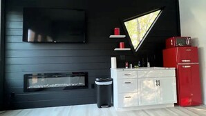 Ein modernes Wohnzimmer mit schwarzer Wand, einer Wand-TV-Anlage, einem Kamin, einem weißen Schrank und einem roten Kühlschrank sowie einem Teppich mit Muster.