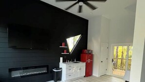 Ein modernes Wohnzimmer mit schwarzer Akzentwand, Deckenventilator, großem Fenster und einem roten und grünen Sofa.