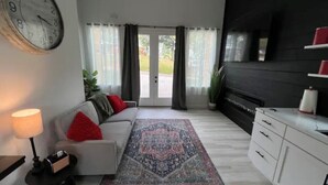 Ein modernes Wohnzimmer mit einem weißen Sofa, einem gemusterten Teppich, einer Uhr und einem Fernseher an einer schwarzen Wand.