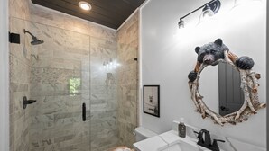 A modern bathroom with a glass-enclosed shower, a white sink with a black faucet, and a bear-themed mirror. - 8 miles to Dollywood-Hot Tub-Game Room-King & Queen Beds-Sleeps up to 6 (Sevierville)