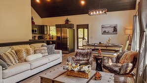 A spacious living room with a large sofa, a coffee table, and a fireplace. There is a kitchen in the background with a refrigerator and cabinets. - 8 miles to Dollywood-Hot Tub-Game Room-King & Queen Beds-Sleeps up to 6 (Sevierville)