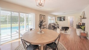 A spacious living area with a large wooden dining table, comfortable seating, and a view of a swimming pool. - Weeki Wachee Pod


 (Spring Hill)