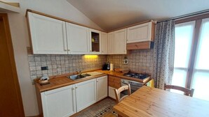 A compact kitchen with white cabinets, a wooden countertop, a stove, and a dining area with a wooden table and chairs. - Bright one-bedroom apartment with panoramic view terrace (Chiesa In Valmalenco)