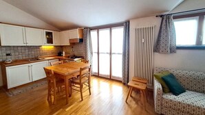 A compact kitchen with wooden cabinets, a dining table, and a sofa. - Bright one-bedroom apartment with panoramic view terrace (Chiesa In Valmalenco)